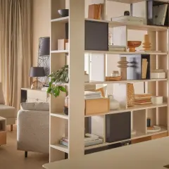 Otwarta regałowa ścianka działowa pozwala jak wydzielić miejsce do pracy w salonie bez stawiania ścianki. Wygodna sofa i zasłony tworzą przytulną atmosferę.