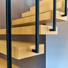 Drewniane stopnie schodów wsparte na czarnym stelażu stalowym. Pokazano, jak przymocować trepy drewniane do stelaża stalowego.