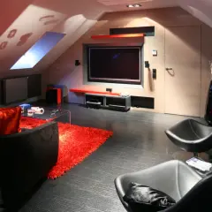 Nowoczesny salon na poddaszu ze skosami. Telewizor zamontowany na ścianie, obok wygodne fotele i kanapa.