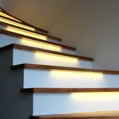 Oświetlenie LED nad klatką schodową z wysokim sufitem: taśmy LED zamontowane pod stopniami tworzą ciepłą, nowoczesną atmosferę.