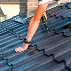 Ręka przykręca dachówkę, pokazując jak uszczelnić stary dach z blachy trapezowej pianą PUR od zewnątrz.