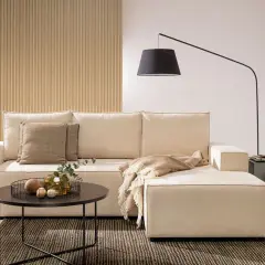 Salon z aneksem bez okna. Jasna kanapa, stolik kawowy, lampa łukowa i dekoracje tworzą przytulną atmosferę.