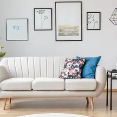 Jasna sofa na nóżkach ułatwia sprzątanie robotem, bo wjedzie pod nią. Wady i zalety tej konfiguracji widać na drewnianej podłodze.