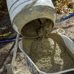 Betoniarka wylewa świeży beton do taczki. Obliczenia i proporcje: ile betonu B20 uzyskamy z worka 25kg suchej mieszanki.