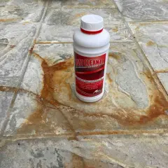 Schody wejściowe z granitu płomieniowanego z plamami rdzy. Butelka środka Rust Cleanze, który pomoże usunąć rdzę.