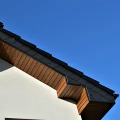 Poddasze domu z drewnianą podbitką, która szybciej psuje się od wilgoci, w kontraście do dachówki.