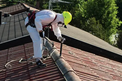 Pracownik w kombinezonie ochronnym usuwa eternit z dachu. To pierwszy krok do wymiany dachu z eternitu krok po kroku, dotacje i utylizacja azbestu.