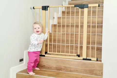 Urocze dziecko przy drewnianej bramce schodowej. Dowiedz się, jak bezpiecznie zamontować bramkę na schodach bez wiercenia w balustradzie.
