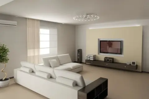 Nowoczesny salon z jasną sofą i telewizorem na tle beżowej ściany. Optyczne wydłużenie niskiego salonu triki z oświetleniem i farbą.