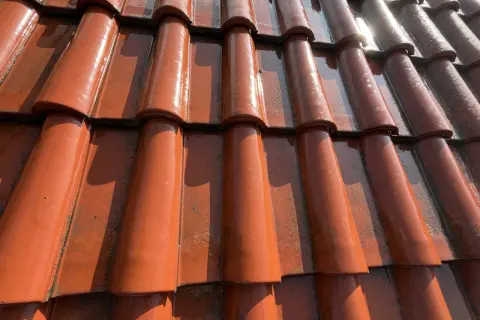 Wilgotne, pomarańczowe dachówki betonowe z widocznymi zaciekami i przebarwieniami, które wyjaśniają, dlaczego dachówka betonowa z czasem traci kolor i obrasta mchem.