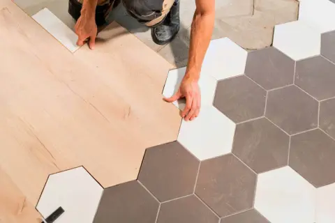 Ręczne łączenie paneli podłogowych z płytkami ceramicznymi w kształcie heksagonów, tworząc płynne przejście bez widocznej listwy progowej.