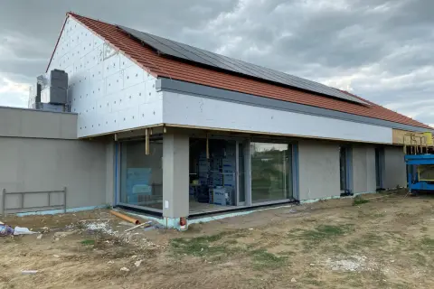Nowoczesna stodoła w budowie, brak okapu dachu. Jak uchronić elewację przed deszczem? Widoczne panele fotowoltaiczne i styropian.