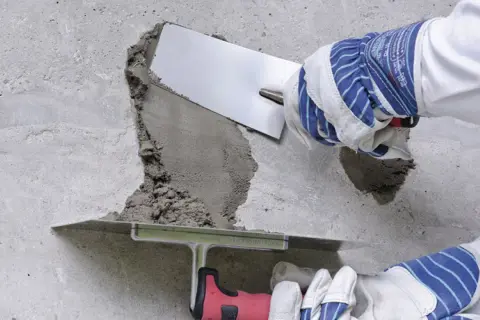 Naprawa betonu: wibrowanie betonu z gruszki zapobiega powstawaniu raków. Użycie kielni do wygładzenia zaprawy.