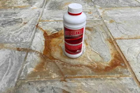 Schody wejściowe z granitu płomieniowanego z plamami rdzy. Butelka środka Rust Cleanze, który pomoże usunąć rdzę.