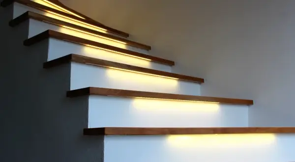 Oświetlenie LED nad klatką schodową z wysokim sufitem: taśmy LED zamontowane pod stopniami tworzą ciepłą, nowoczesną atmosferę.