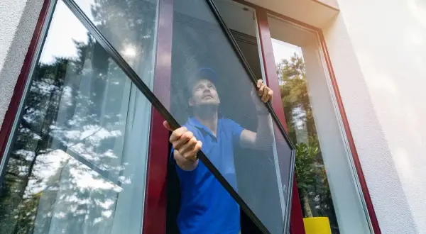 Mężczyzna montuje moskitierę ramkową. Dowiedz się, jak zamontować moskitierę ramkową żeby nie odpadała przy wietrze, by cieszyć się świeżym powietrzem bez owadów.