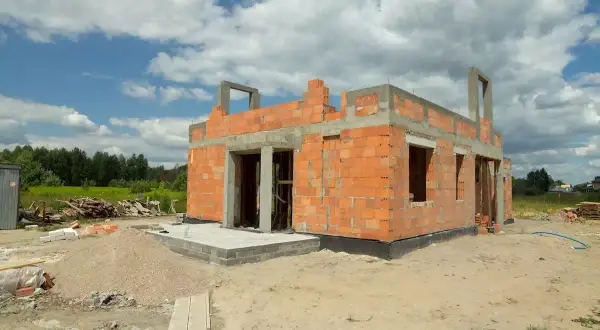 Budowa domu z pustaka żużlowego: dlaczego odchodzi się od tego materiału? Widok na budowę domu z cegły, z widocznymi materiałami budowlanymi.