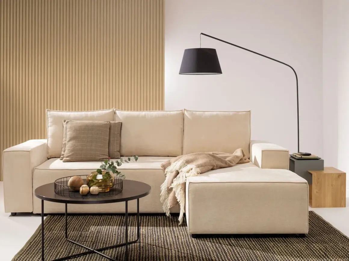 Salon z aneksem bez okna. Jasna kanapa, stolik kawowy, lampa łukowa i dekoracje tworzą przytulną atmosferę.