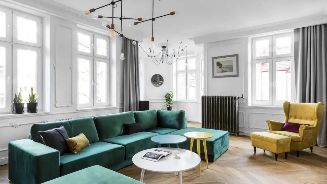 Elegancki salon z butelkową zielenią kanapy. Połączono ją z żółtym fotelem i stolikami, tworząc przytulną przestrzeń.