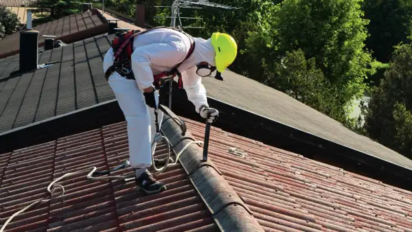 Pracownik w kombinezonie ochronnym usuwa eternit z dachu. To pierwszy krok do wymiany dachu z eternitu krok po kroku, dotacje i utylizacja azbestu.